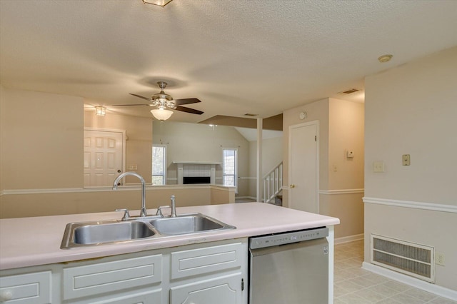 kitchen featuring visible vents, a tiled fireplace, stainless steel dishwasher, a ceiling fan, and a sink