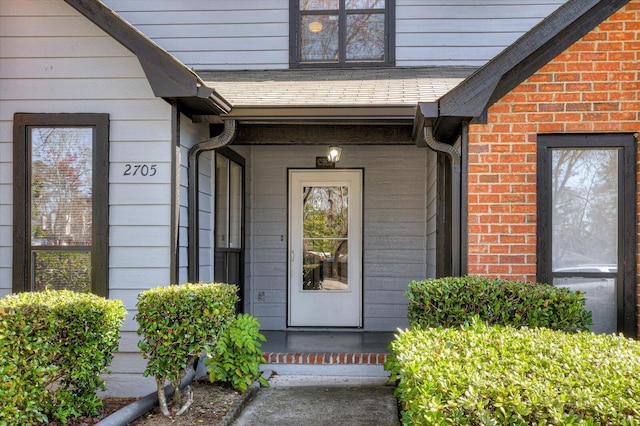 doorway to property with brick siding and roof with shingles