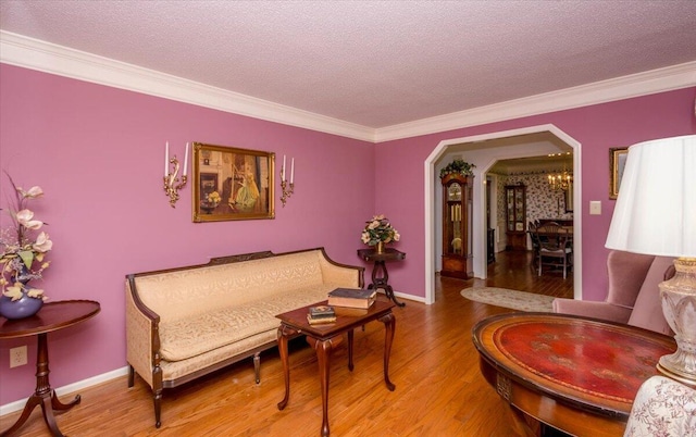 sitting room featuring crown molding, arched walkways, wood finished floors, and a textured ceiling
