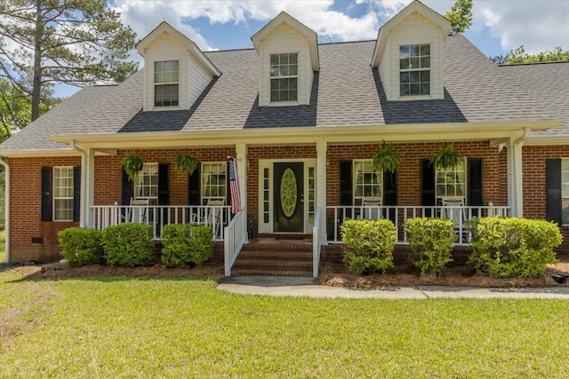 cape cod home featuring covered porch, brick siding, a front yard, and roof with shingles