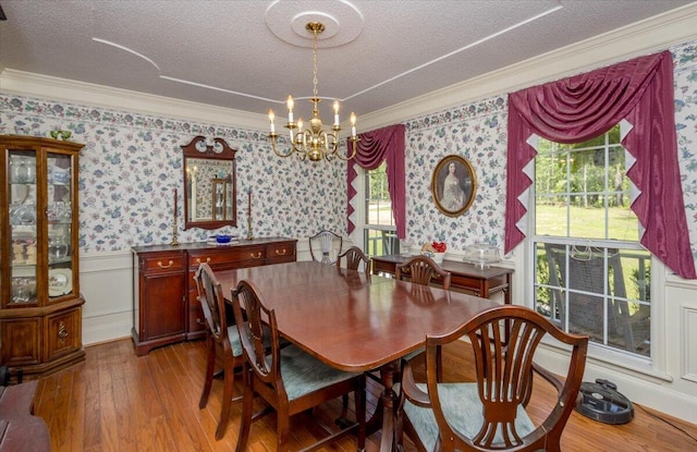 dining area with crown molding, an inviting chandelier, wallpapered walls, and wood finished floors
