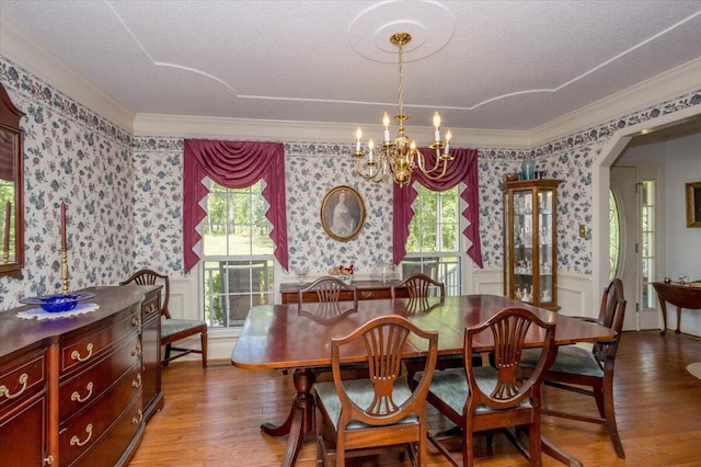 dining space with a chandelier, a healthy amount of sunlight, crown molding, and wallpapered walls