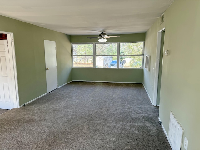 unfurnished room with dark carpet, visible vents, and a ceiling fan