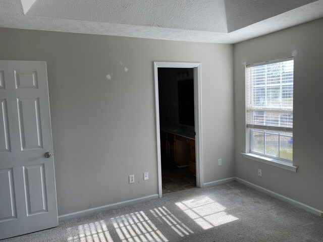 unfurnished bedroom with ensuite bath, a spacious closet, carpet, and a textured ceiling