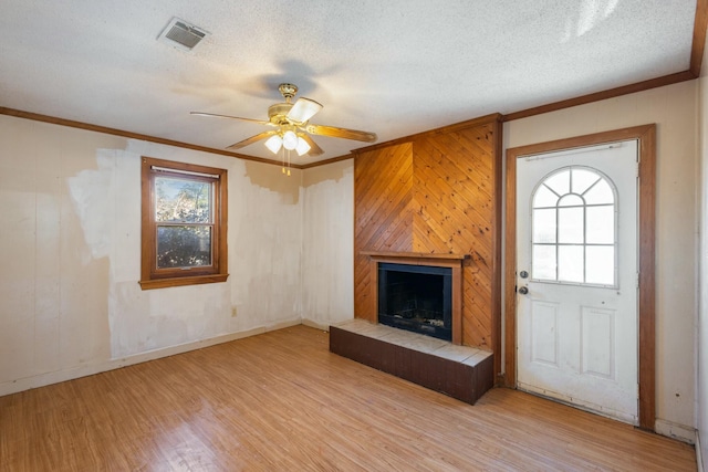 unfurnished living room featuring crown molding, a tiled fireplace, light hardwood / wood-style flooring, and a textured ceiling