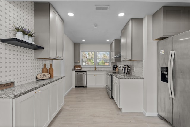 kitchen with wall chimney exhaust hood, light stone counters, stainless steel appliances, and tasteful backsplash