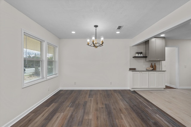 unfurnished dining area with a textured ceiling, dark hardwood / wood-style floors, and an inviting chandelier