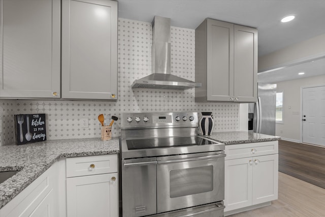 kitchen with light stone countertops, wall chimney exhaust hood, light hardwood / wood-style floors, and appliances with stainless steel finishes