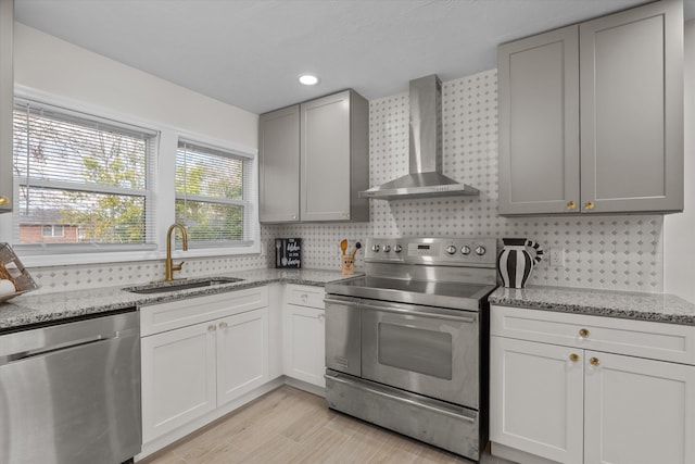 kitchen featuring light stone countertops, sink, wall chimney exhaust hood, backsplash, and appliances with stainless steel finishes