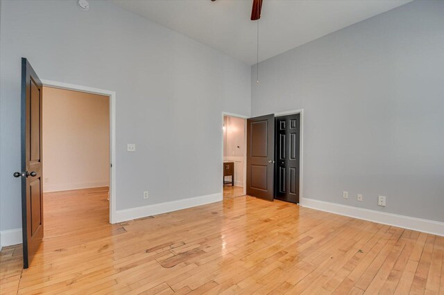 unfurnished bedroom featuring light wood-type flooring, a towering ceiling, and ceiling fan