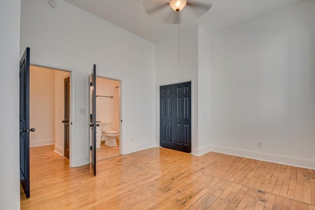 unfurnished bedroom featuring a towering ceiling, ensuite bath, ceiling fan, light hardwood / wood-style flooring, and a closet