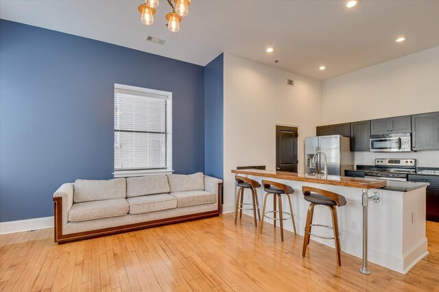 kitchen featuring appliances with stainless steel finishes, light wood-type flooring, a breakfast bar, a kitchen island with sink, and an inviting chandelier