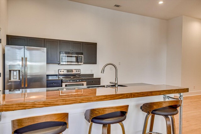 kitchen with a kitchen bar, appliances with stainless steel finishes, light wood-type flooring, and sink