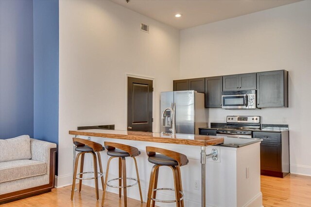 kitchen with kitchen peninsula, a kitchen breakfast bar, a towering ceiling, stainless steel appliances, and light hardwood / wood-style floors