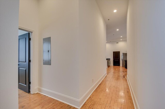 hallway with electric panel, light hardwood / wood-style floors, and a high ceiling