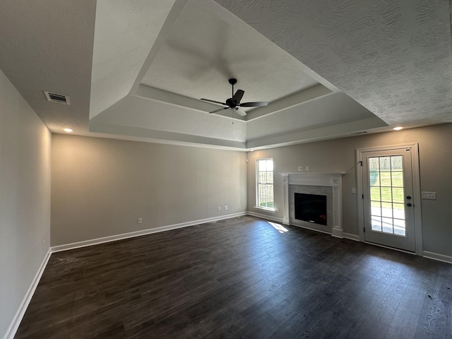 unfurnished living room with a textured ceiling, a raised ceiling, ceiling fan, dark hardwood / wood-style floors, and a tiled fireplace