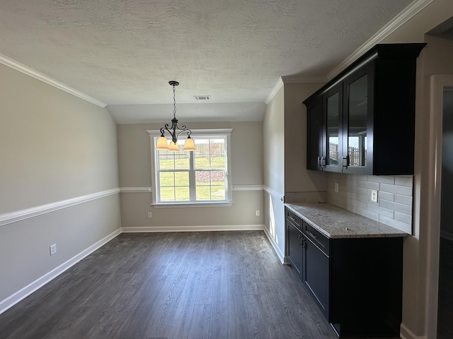 kitchen featuring dark wood-type flooring, hanging light fixtures, decorative backsplash, light stone countertops, and a notable chandelier