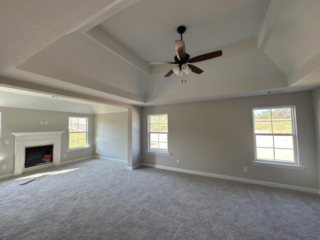 unfurnished living room with a tray ceiling, a wealth of natural light, ceiling fan, and carpet floors