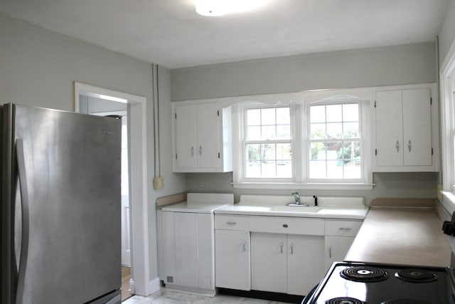 kitchen featuring sink, range, white cabinets, and stainless steel refrigerator