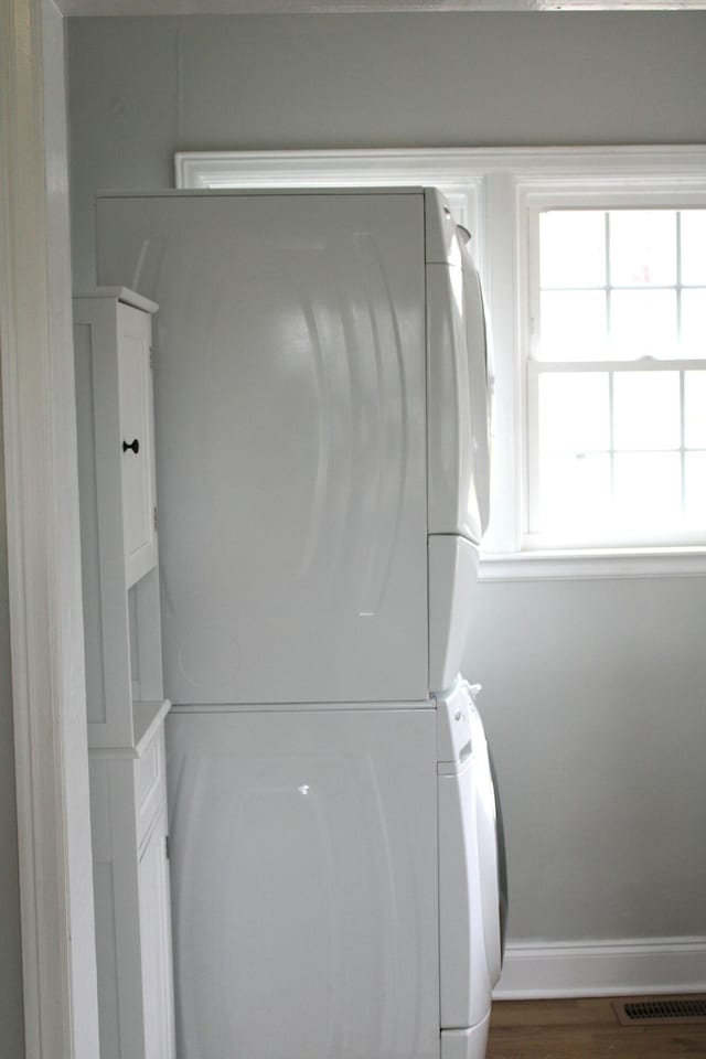 clothes washing area with dark wood-type flooring and stacked washer and clothes dryer