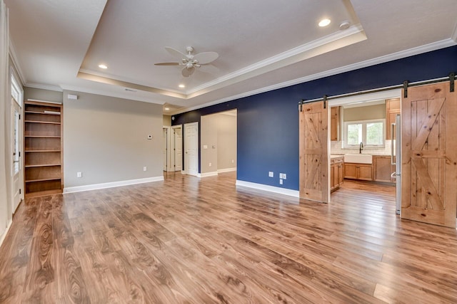 interior space featuring ensuite bathroom, crown molding, a raised ceiling, ceiling fan, and a barn door