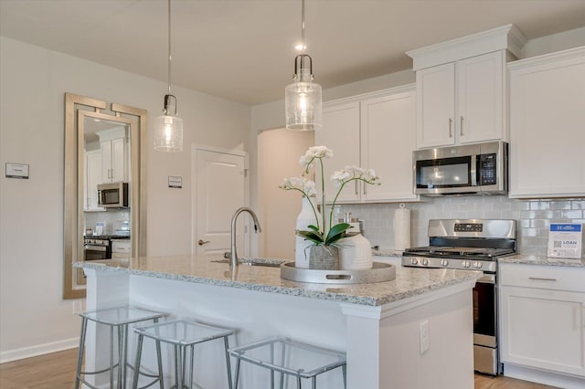 kitchen featuring white cabinetry, stainless steel appliances, backsplash, decorative light fixtures, and a kitchen island with sink