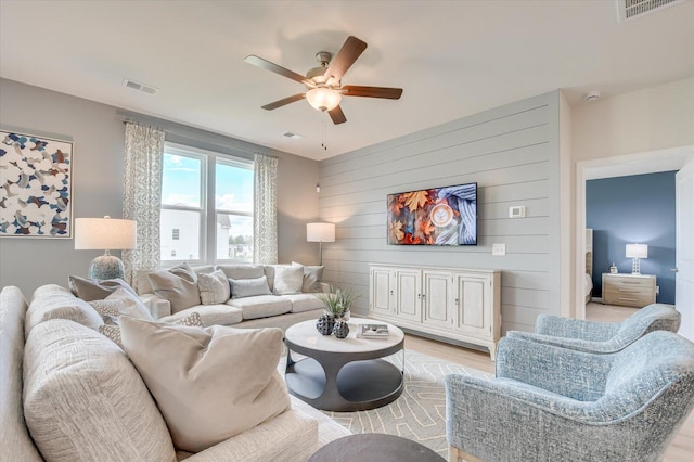 living room with ceiling fan, light hardwood / wood-style floors, and wooden walls