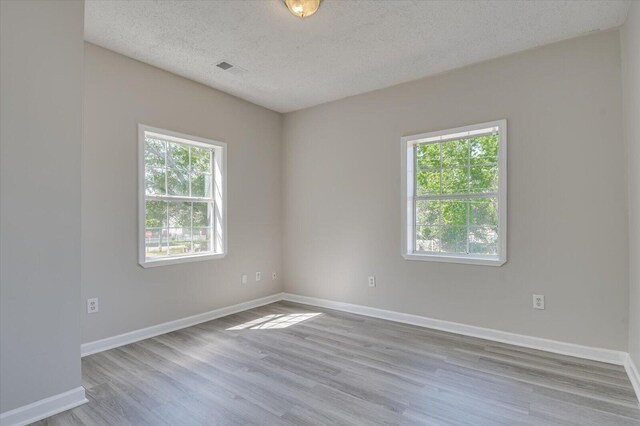 unfurnished room featuring a textured ceiling, wood finished floors, baseboards, and plenty of natural light