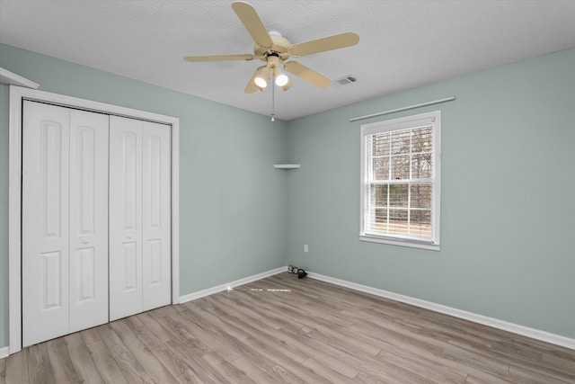 unfurnished bedroom featuring a textured ceiling, light hardwood / wood-style flooring, a closet, and ceiling fan