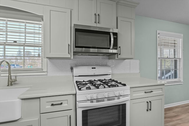 kitchen featuring sink, decorative backsplash, light hardwood / wood-style floors, and white gas range oven