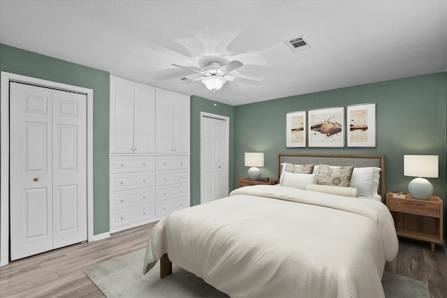 bedroom with two closets, light hardwood / wood-style flooring, a textured ceiling, and ceiling fan