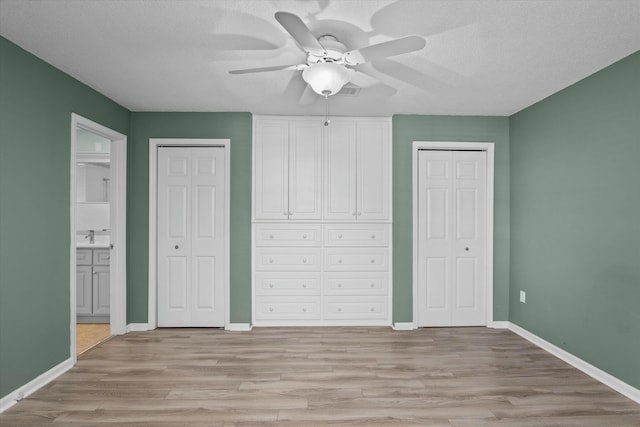 unfurnished bedroom featuring multiple closets, connected bathroom, a textured ceiling, and light hardwood / wood-style flooring