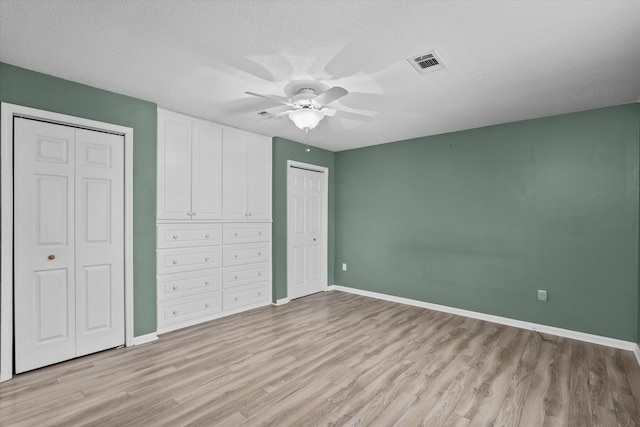 unfurnished bedroom featuring ceiling fan, light hardwood / wood-style floors, a textured ceiling, and two closets