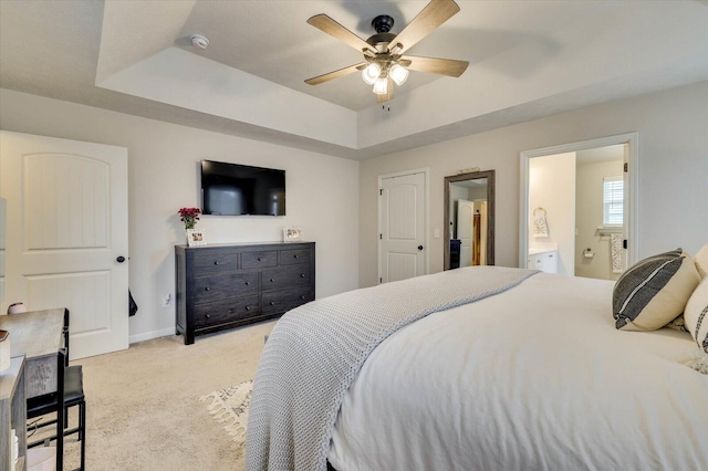 bedroom featuring a tray ceiling, ensuite bath, ceiling fan, and light colored carpet