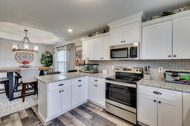 kitchen featuring hanging light fixtures, stainless steel appliances, hardwood / wood-style floors, decorative backsplash, and white cabinets