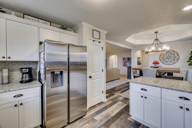 kitchen featuring white cabinets, stainless steel refrigerator with ice dispenser, decorative backsplash, light stone countertops, and a tray ceiling