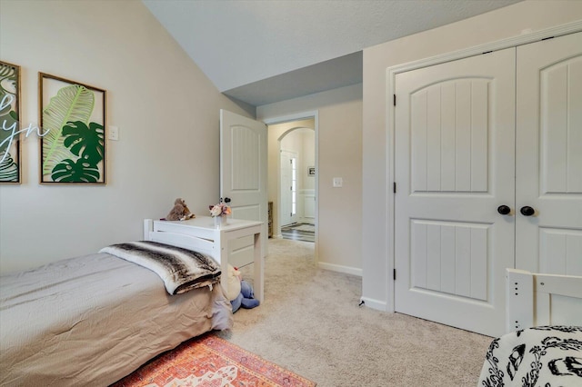 bedroom featuring light colored carpet, vaulted ceiling, and a closet