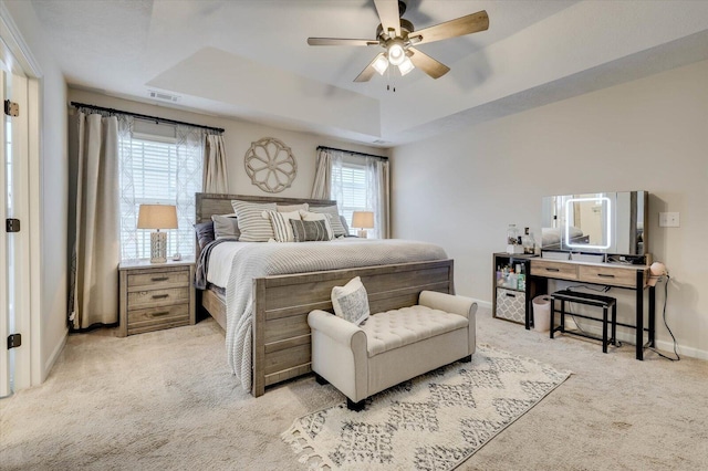 carpeted bedroom featuring ceiling fan, multiple windows, and a tray ceiling