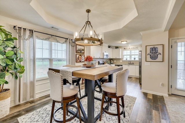 dining area featuring dark hardwood / wood-style flooring, a raised ceiling, crown molding, sink, and an inviting chandelier