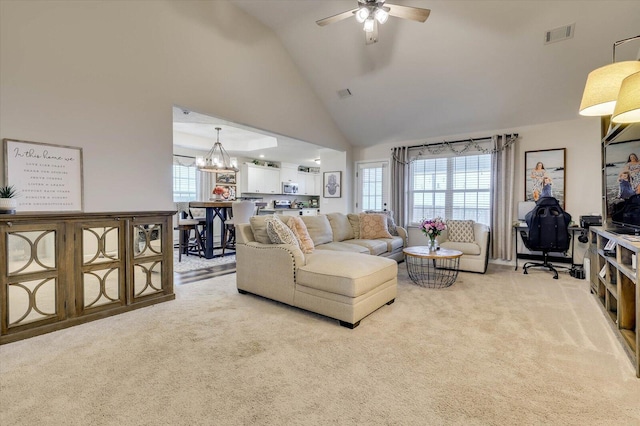 carpeted living room featuring ceiling fan with notable chandelier and high vaulted ceiling