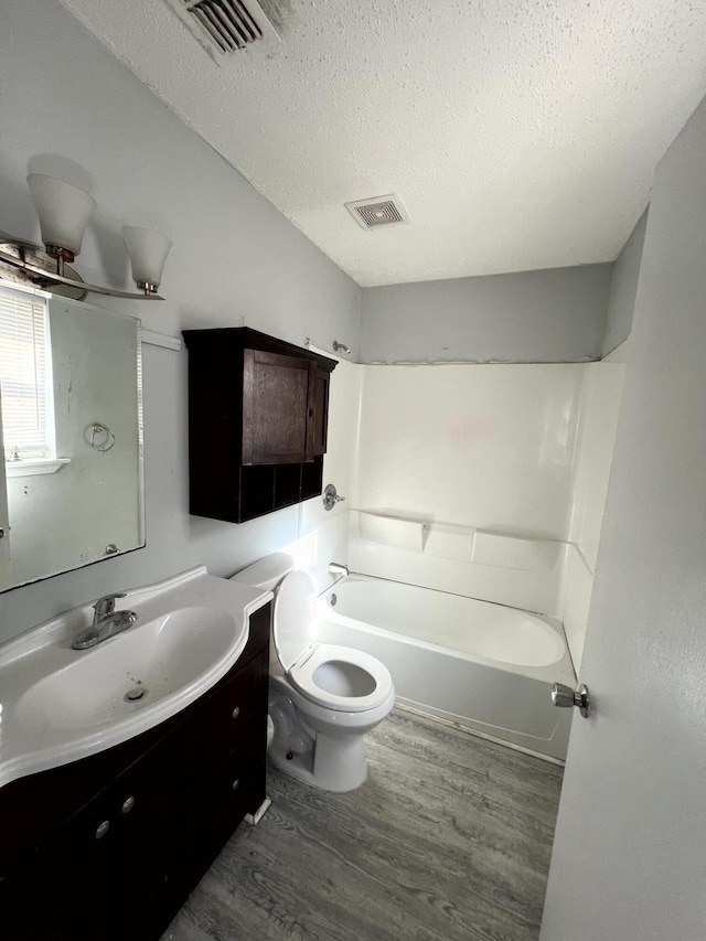 full bathroom with bathing tub / shower combination, hardwood / wood-style floors, a textured ceiling, toilet, and vanity