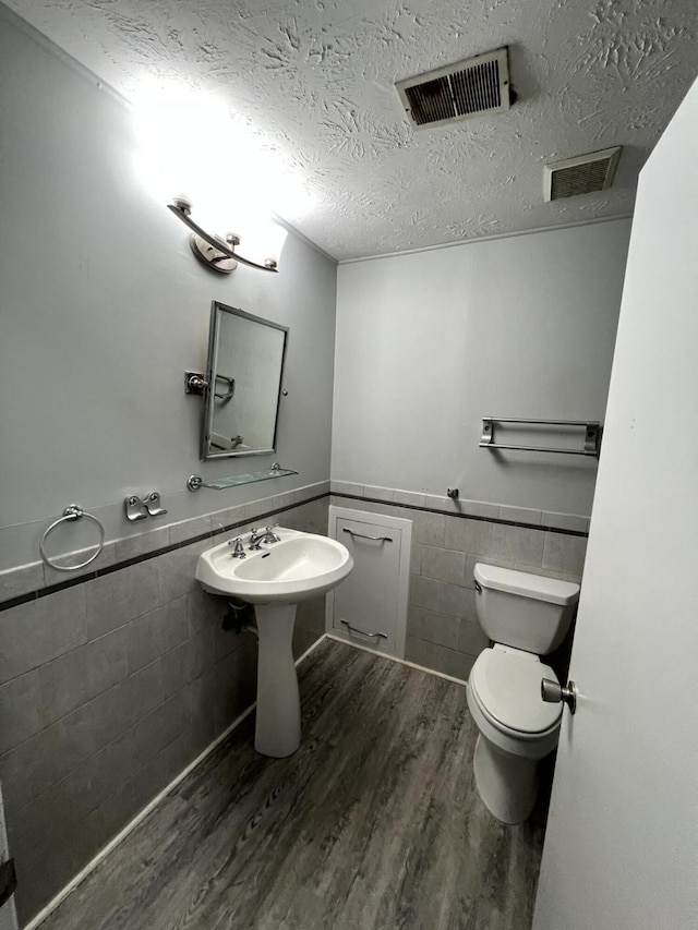 bathroom featuring hardwood / wood-style flooring, toilet, tile walls, and a textured ceiling