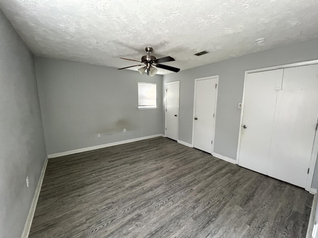 unfurnished bedroom featuring a textured ceiling, dark hardwood / wood-style floors, ceiling fan, and multiple closets