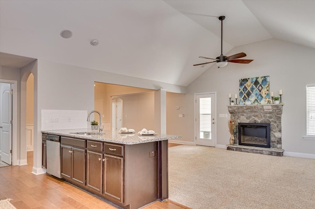 kitchen with a sink, open floor plan, light stone counters, a stone fireplace, and stainless steel dishwasher