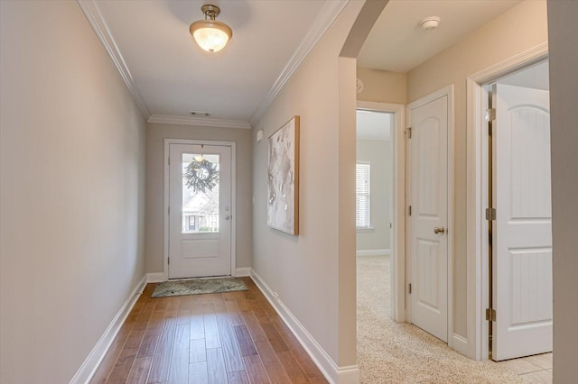 doorway to outside featuring wood finished floors, visible vents, baseboards, arched walkways, and ornamental molding