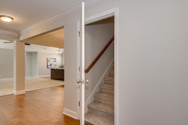 stairway with wood finished floors, baseboards, and ornamental molding