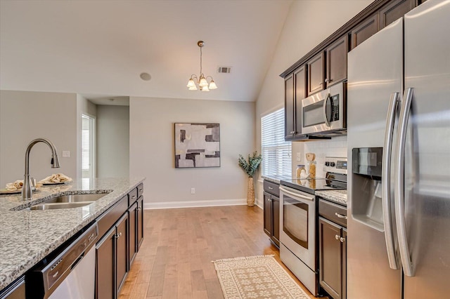 kitchen featuring light wood-type flooring, lofted ceiling, light stone counters, appliances with stainless steel finishes, and a sink