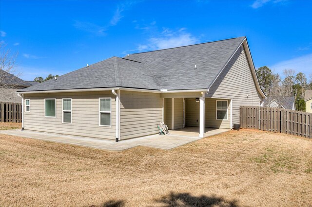 back of property with a lawn, a shingled roof, a patio, and fence