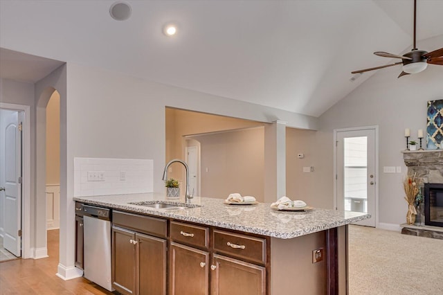 kitchen featuring a sink, light stone counters, a fireplace, dishwasher, and vaulted ceiling