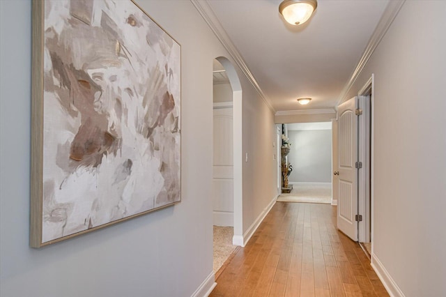 hall featuring crown molding, light wood-style flooring, baseboards, and arched walkways